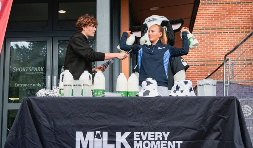 Two students and Moovit the cow mascot at the Milk Every Moment dairy stand.